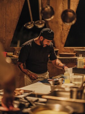 A chef in a kitchen with wooden walls, stainless steel appliances, and various cooking utensils. - Paradero Todos Santos (Todos Santos)