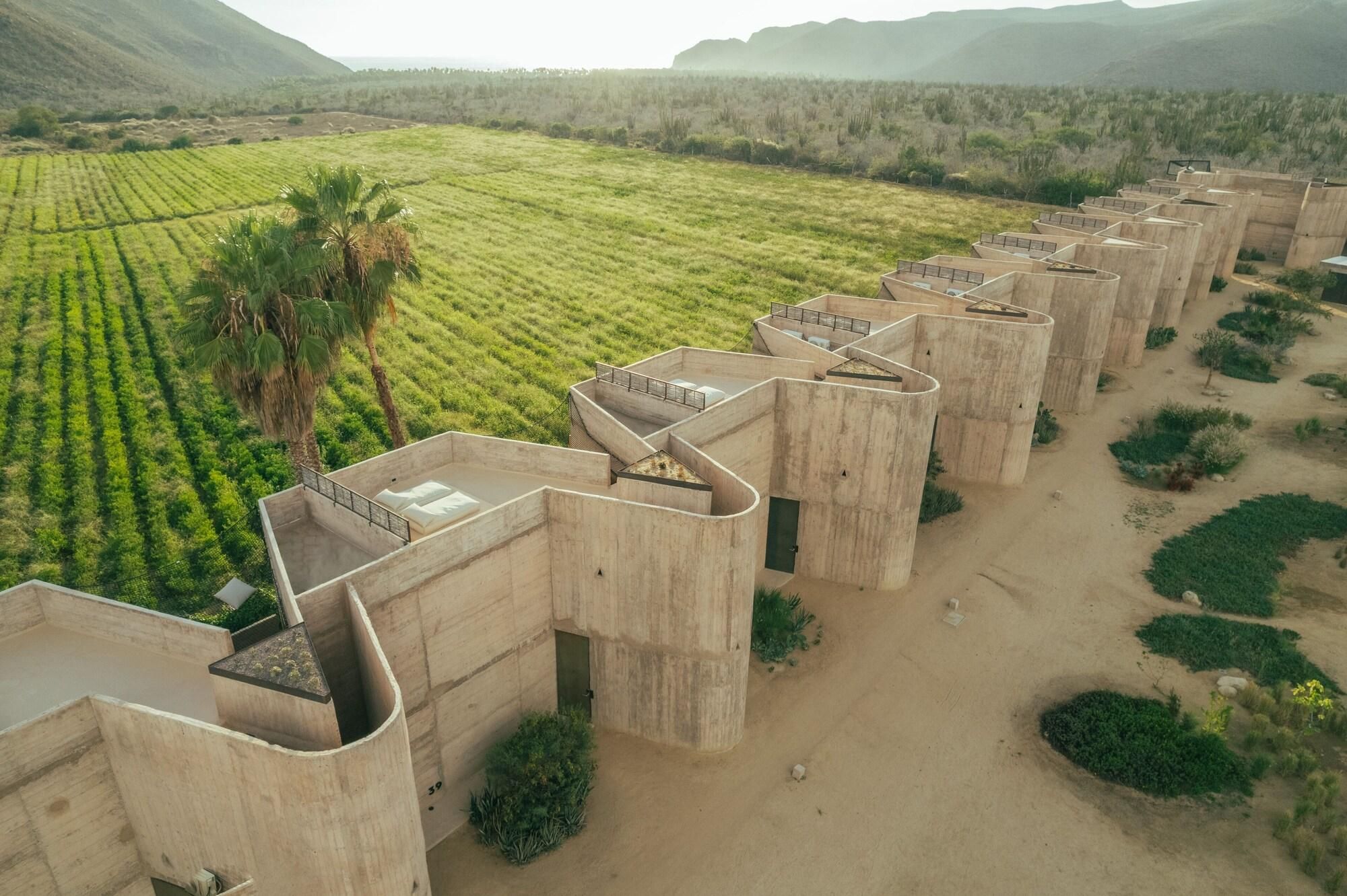 A series of concrete structures with flat roofs, surrounded by agricultural fields and sparse vegetation.