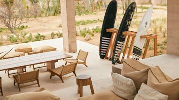 An outdoor seating area with a table, chairs, a sofa, and surfboards.