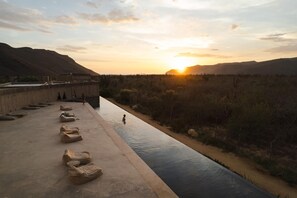 Une rivière avec une promenade en béton, une personne dans l’eau et un coucher de soleil en arrière-plan.