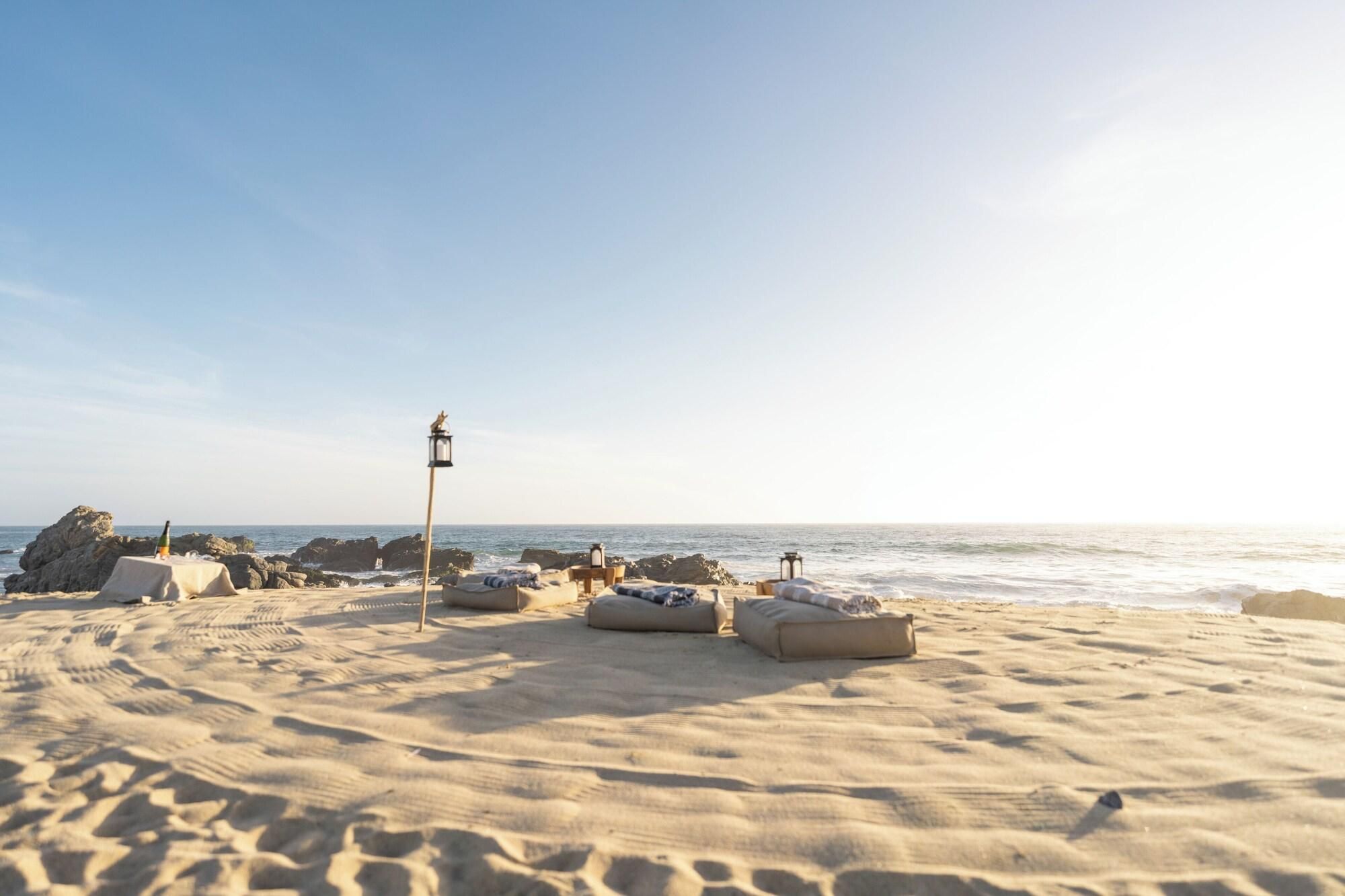 A beach with a row of sun loungers, a lamp post, and a bottle of champagne on a table.