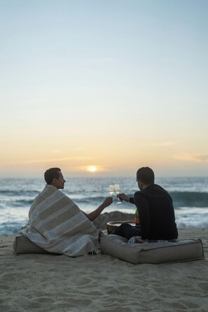 Two people sitting on a beach blanket facing the ocean, holding glasses. - Paradero Todos Santos (Todos Santos)