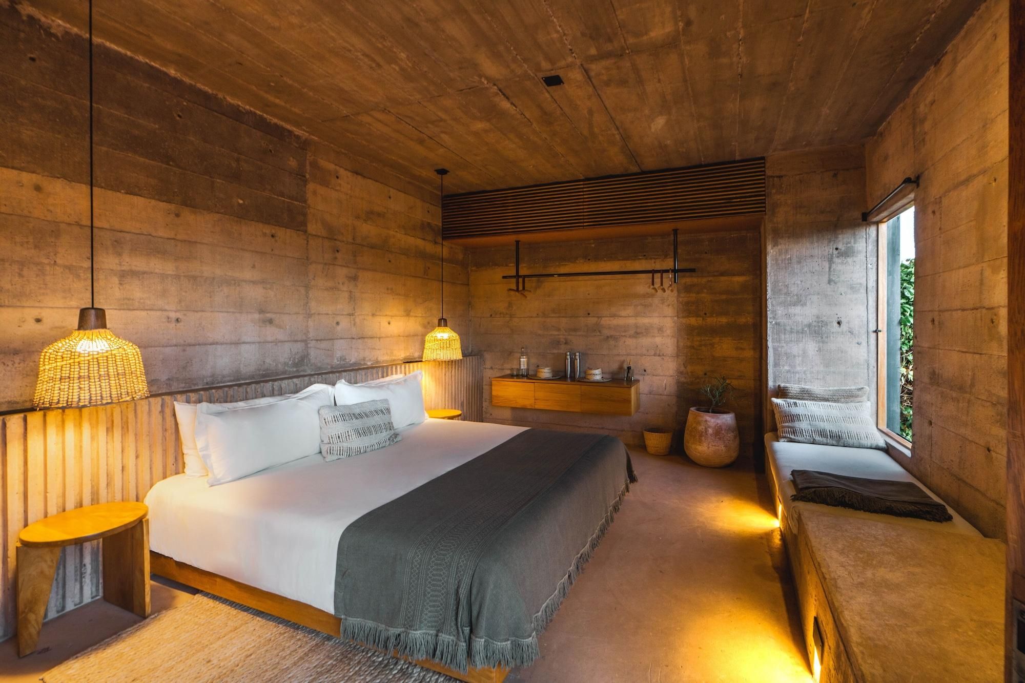 A bedroom with a bed, bedside tables, a window, and a wooden ceiling.