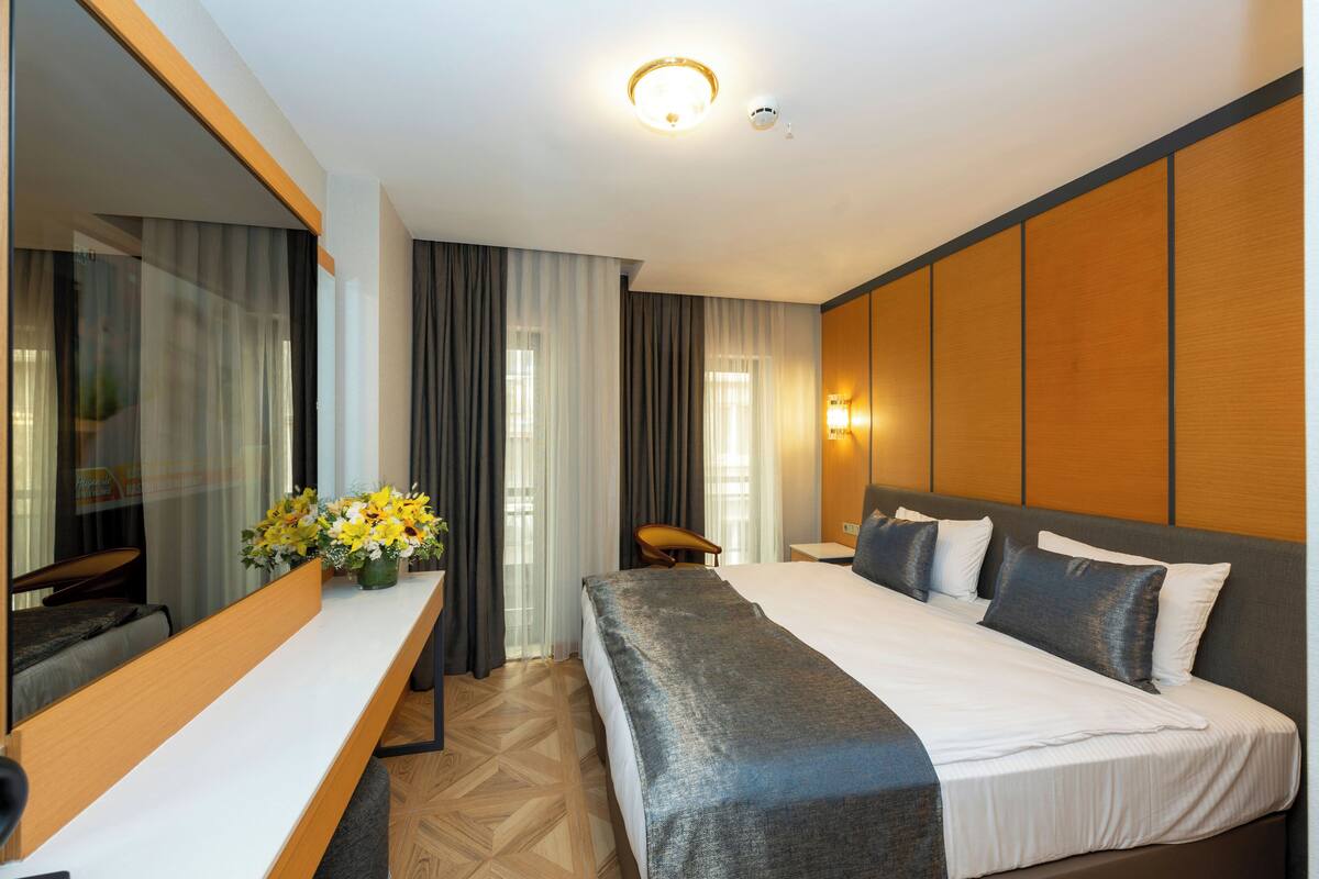 Habitación de hotel con una cama grande, un escritorio con silla, un espejo y una lámpara fijada a la pared.