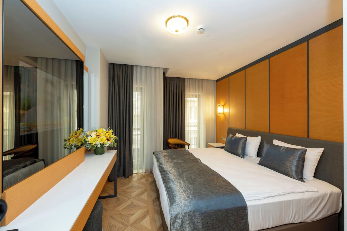 Hotellihuone, jossa on suuri sänky, työpöytä tuolilla, peili ja seinään kiinnitetty valaisin.