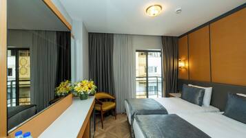 Habitación de hotel con dos camas, un escritorio, una silla, un espejo grande y una ventana con cortinas.