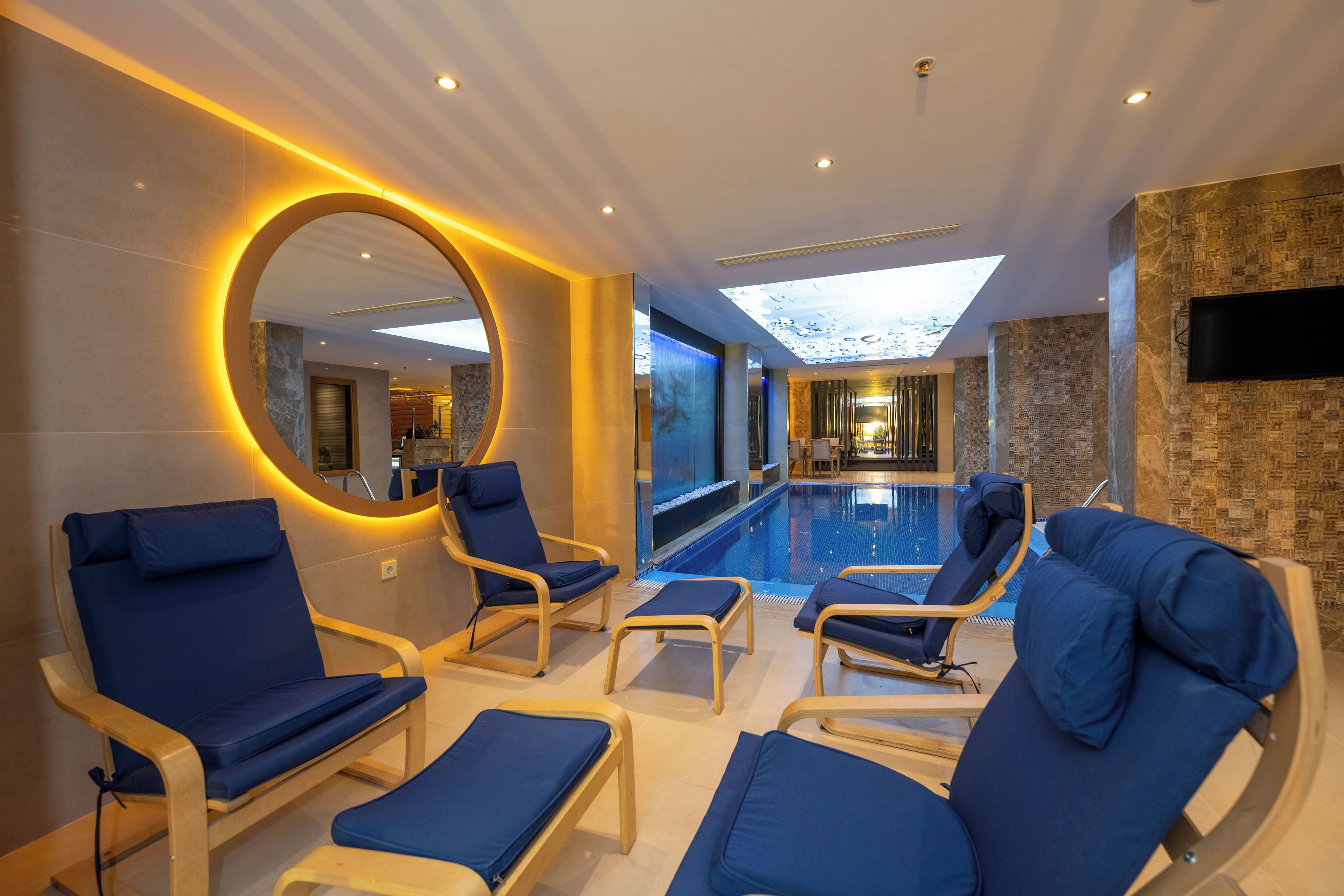 A modern indoor pool area with blue lounge chairs and a large mirror.