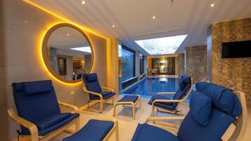 A modern indoor pool area with blue lounge chairs and a large mirror.