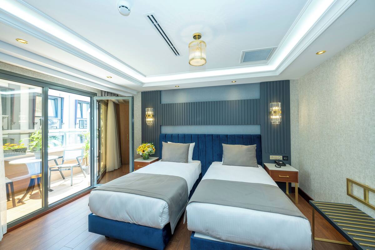 Habitación de hotel con dos camas, un ventanal grande, un balcón y un diseño de techo moderno.