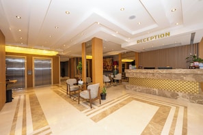 Een hotel receptie met een receptiebalie, zithoek, liften en een vloer met patroon.