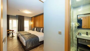 Habitación de hotel con cama doble, un escritorio con silla, una mesita con un florero y un baño con lavabo y espejo.