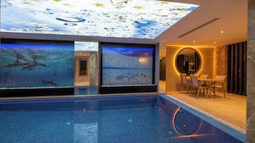 Una piscina interior moderna amb una projecció al sostre de gotes d'aigua i escenes aquàtiques, una zona de seients amb una taula rodona i un gran mirall a la paret.