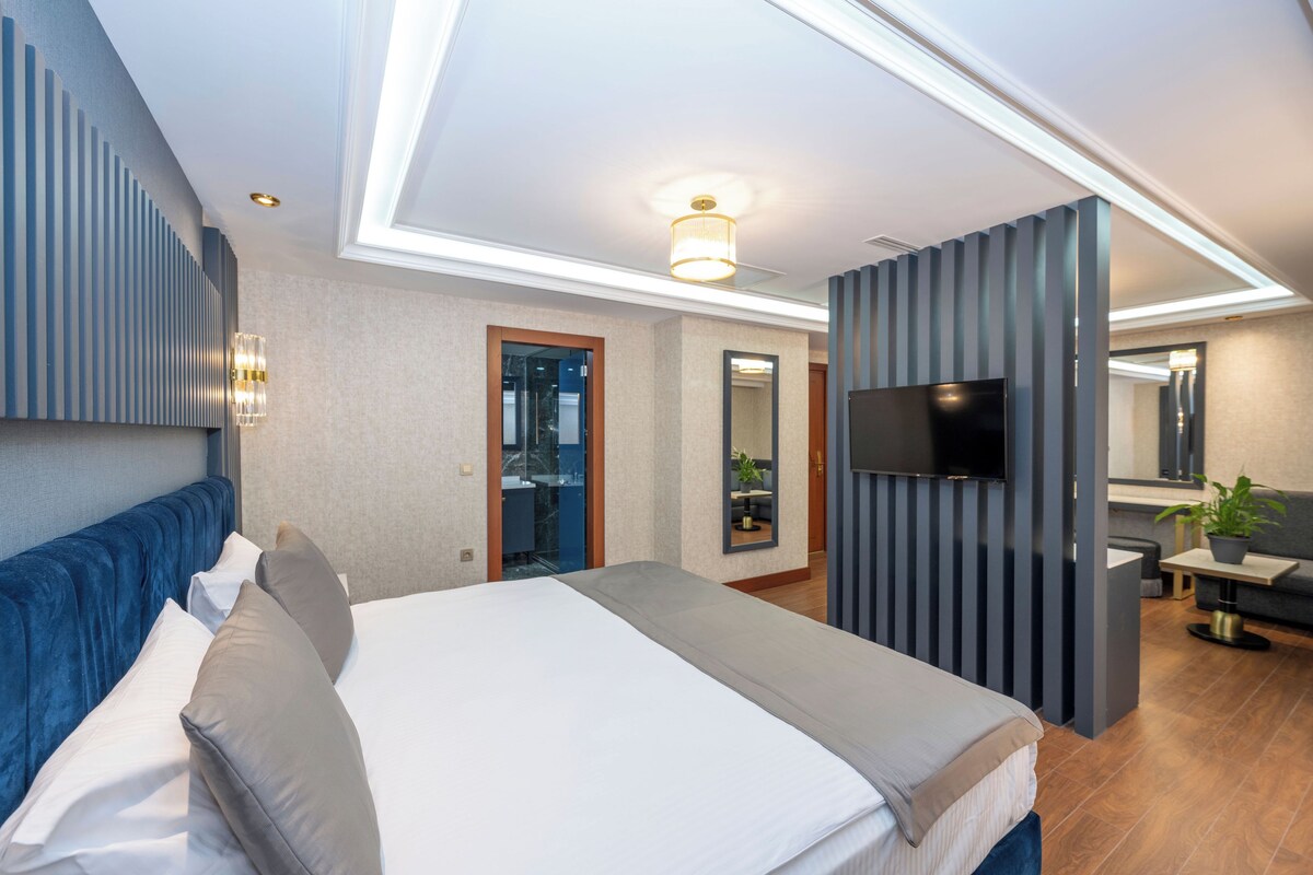 A modern hotel room with a large bed, a TV, a desk, and a bathroom visible through a door.