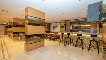 Un bar moderno con barra alta, taburetes y una zona de estar con mesas y sillas.