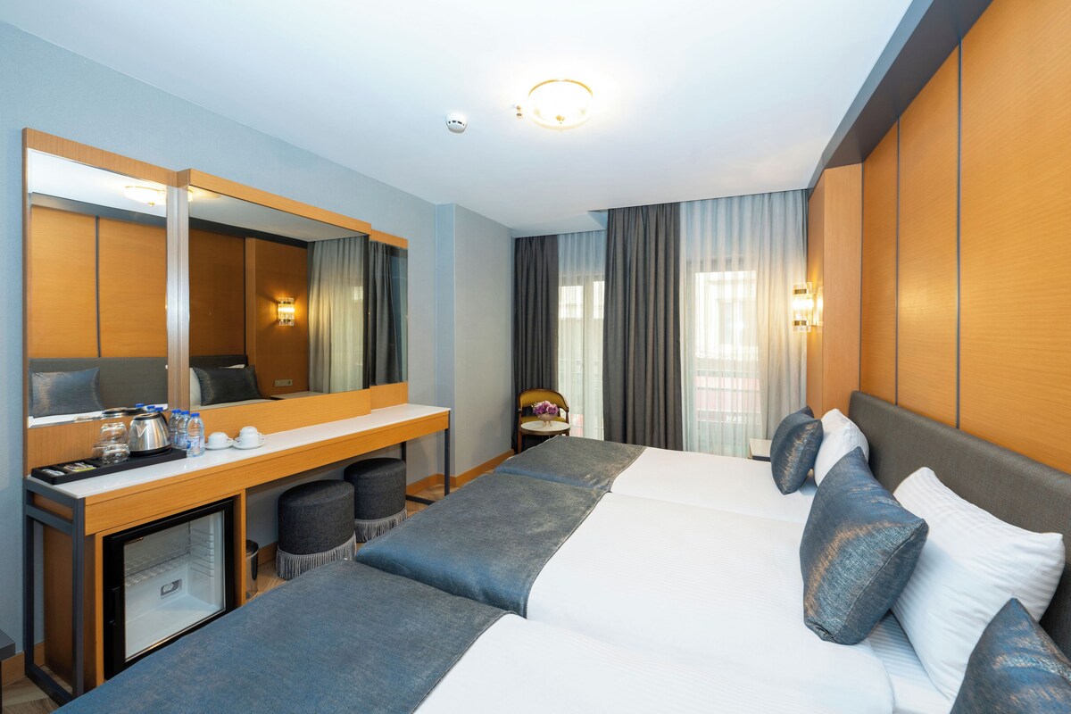 A hotel room with a bed, a desk, a chair, a small table, and a mirror.
