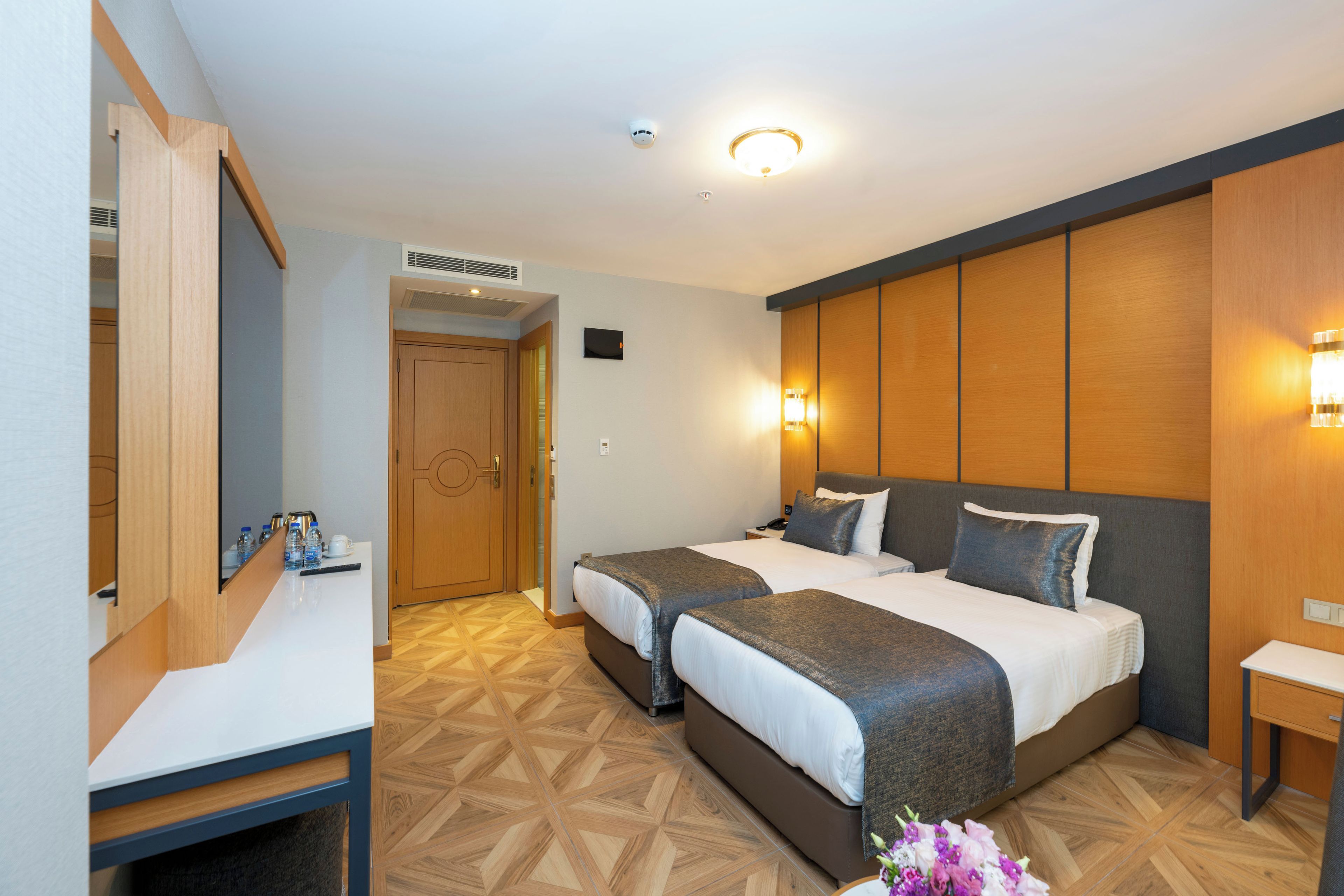 Habitación de hotel con dos camas, un escritorio, un espejo y la puerta del baño.