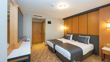Habitación de hotel con dos camas, un escritorio, un espejo y la puerta del baño.