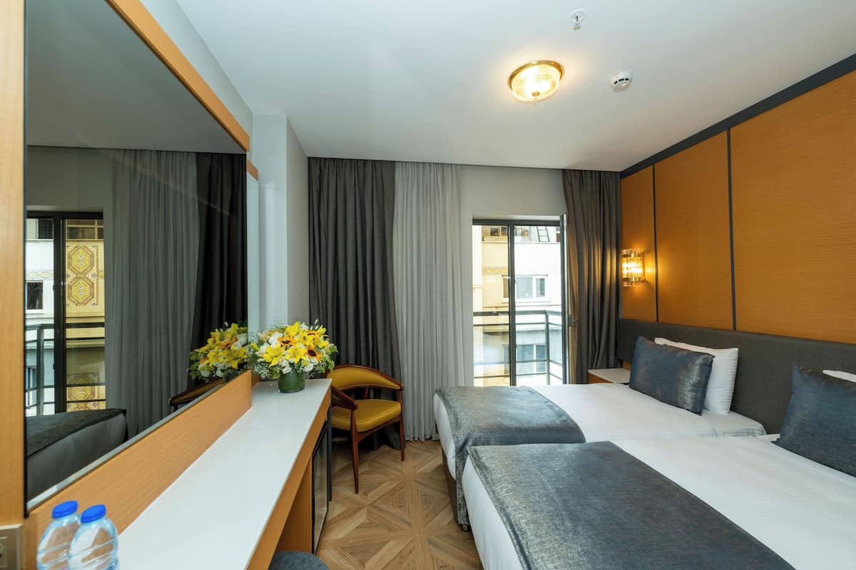 Habitación de hotel con dos camas, un escritorio, una silla, un espejo grande y una ventana con cortinas.