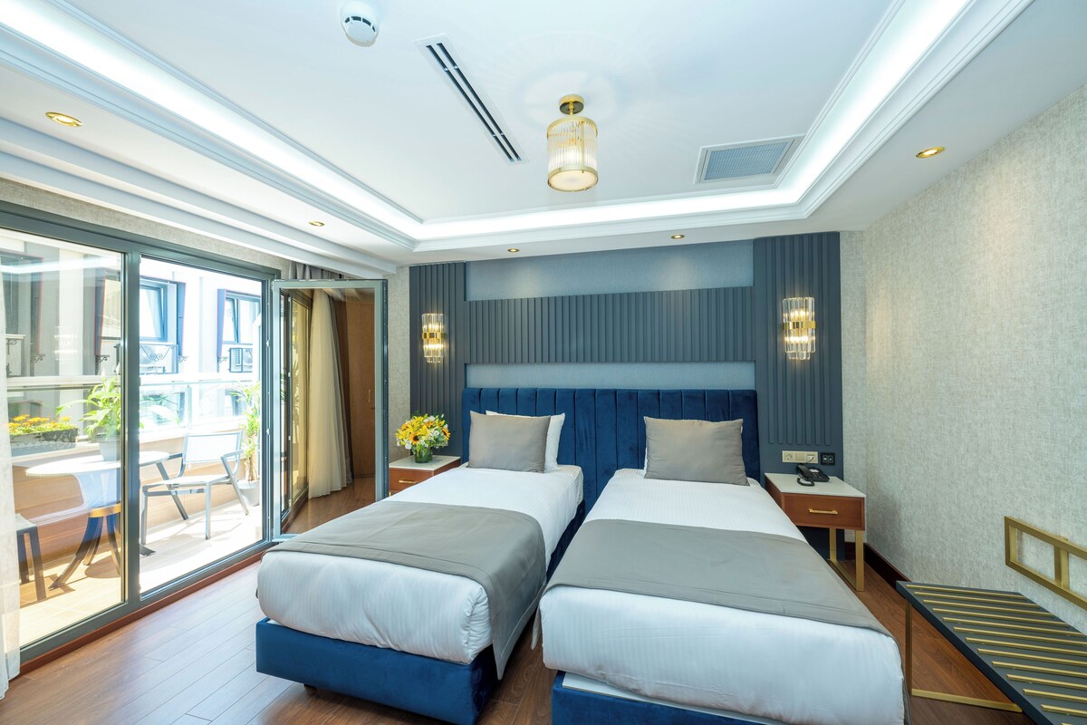 A hotel room with two beds, a large window, a balcony, and a modern ceiling design.