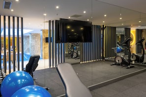 A modern gym with exercise equipment, a large mirror, and a television. - Freya Hotel (Istanbul)