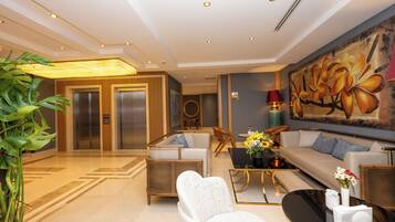 Un hall con mostrador de recepción, zona de estar, ascensores y un cuadro grande con motivos florales.