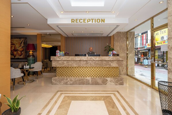 A reception area with a marble counter, a receptionist, and a view of the street outside. - Freya Hotel (Istanbul)