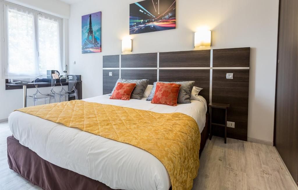 A hotel room with a large bed, a desk with a chair, and two wall-mounted lamps.