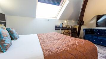 Un dormitorio con cama, escritorio, silla, sofá azul y tragaluz.