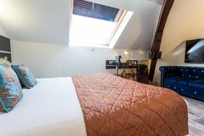 Un dormitorio con cama, escritorio, silla, sofá azul y tragaluz.