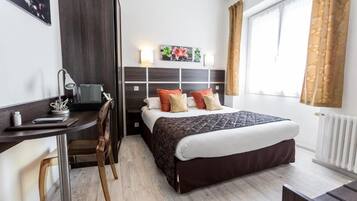 A modern hotel room with a bed, bedside table, desk, chair, and a window with curtains.