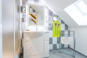 A modern bathroom with a skylight, a white sink, a mirror, and a towel rack.