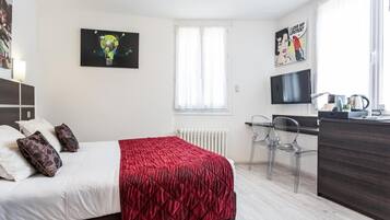 Una habitación de hotel con cama, escritorio, silla, radiador y televisor.