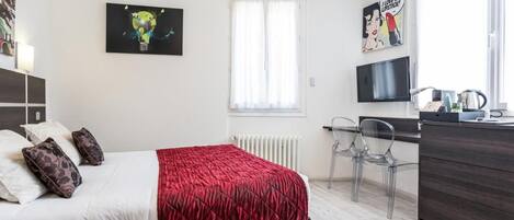 Une chambre d’hôtel avec un lit, un bureau, une chaise, un radiateur et un téléviseur.