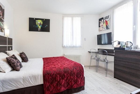 A hotel room with a bed, a desk, a chair, a radiator, and a TV. - Logis Hôtel du Centre (Rocamadour)
