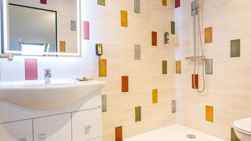 Un baño con lavamanos blanco, espejo y ducha.