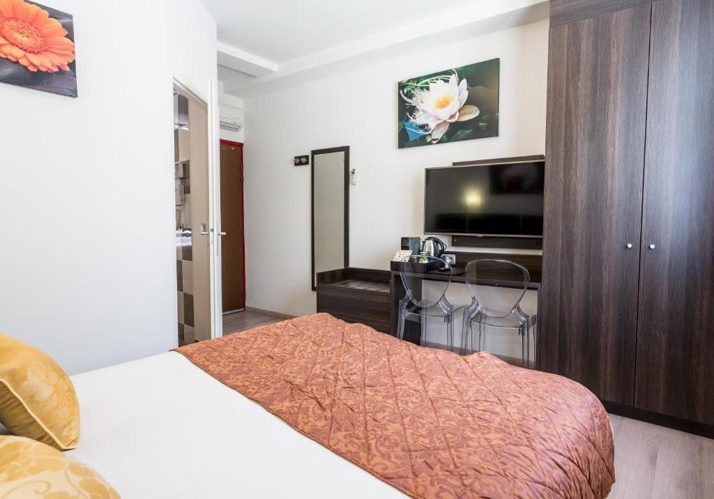 A hotel room with a bed, a desk with a chair, a TV, and a wardrobe.