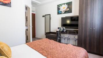 A hotel room with a bed, a desk with a chair, a TV, and a wardrobe.