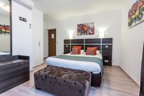 A bedroom with a bed, a bench, a headboard, a wall-mounted artwork, and a door. - Logis Hôtel du Centre (Rocamadour)
