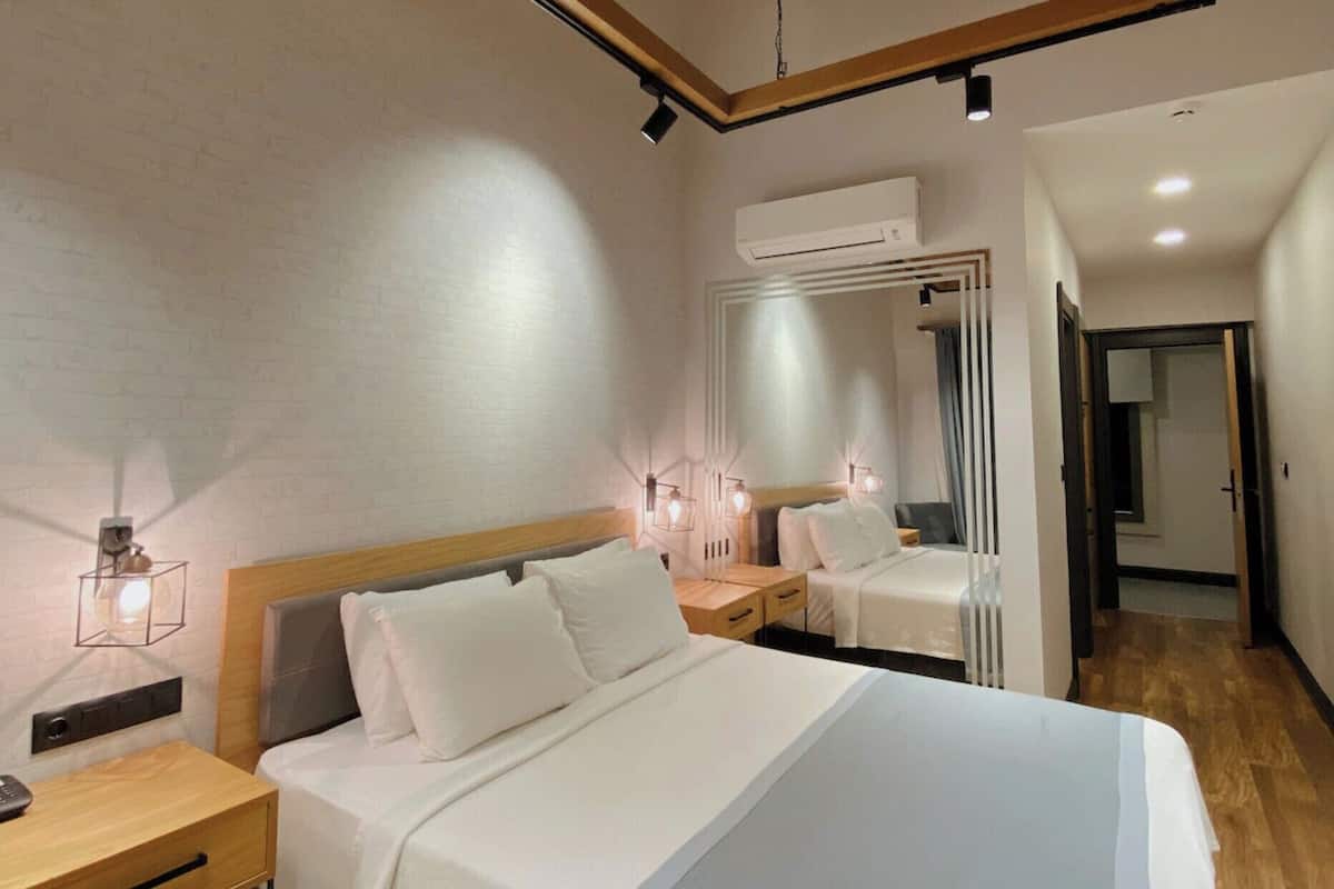A modern hotel room with a large bed, bedside tables, a mirror, and a ceiling-mounted air conditioner.