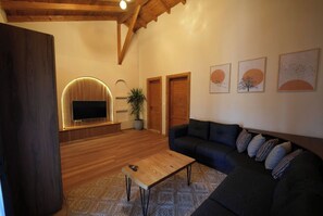 Ein Wohnzimmer mit Holzboden, einer Couch, einem Couchtisch, einem Fernseher und gerahmten Kunstwerken an der Wand.