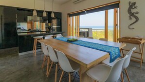 A modern kitchen with a dining area, large windows, and a view of the sea. - Villa K by Zuzu (Selong Belanak)