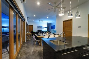 A modern kitchen with a central island, a dining area, and a ceiling fan. - Villa K by Zuzu (Selong Belanak)
