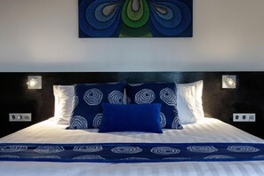 Ein Bett mit einem gemusterten Überwurf, Kissen mit einem Rundmuster und ein Wandbild darüber.