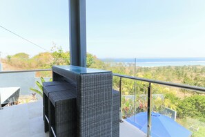 Ein Balkon mit Meerblick, ein Korbstuhl und ein blauer Sonnenschirm.