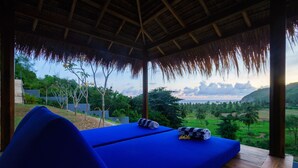 A room with a blue bed, a view of the landscape, and a thatched roof. - Villa K by Zuzu (Selong Belanak)