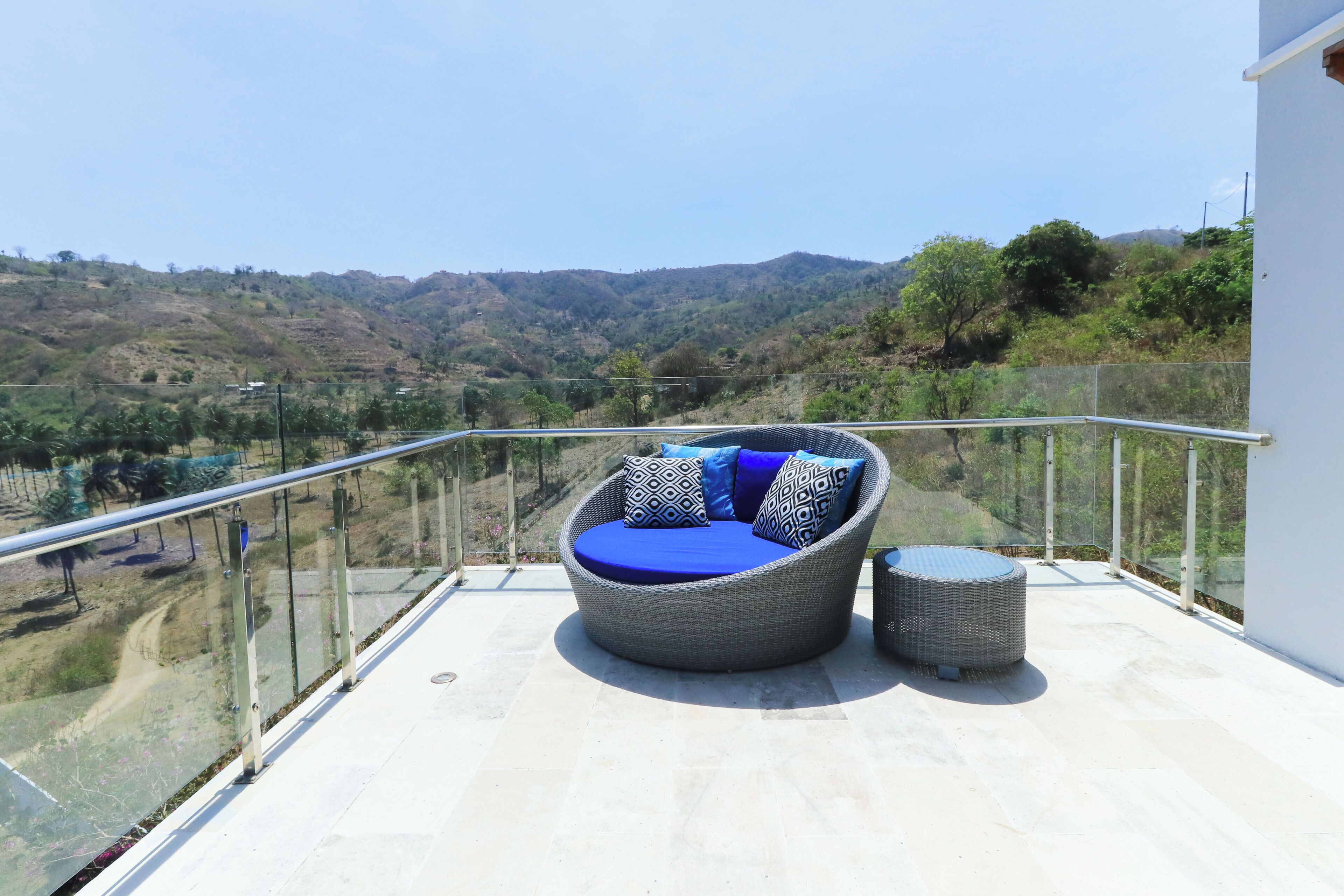 Ein Balkon mit einer Rattan-Couch und Hocker, der einen Blick auf eine hügelige Landschaft bietet.