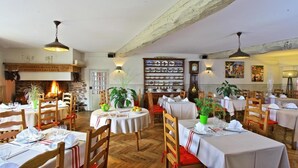 A restaurant with wooden beams, a fireplace, and multiple tables set for dining. - Logis Hotel Du Fronton-agian (Itxassou)