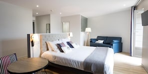 A modern hotel room with a bed, a sofa, a round table, and a TV. - Logis Hotel Du Fronton-agian (Itxassou)