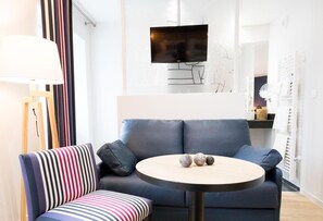 A modern living room with a sofa, a round table, a television, and a lamp. - Logis Hotel Du Fronton-agian (Itxassou)