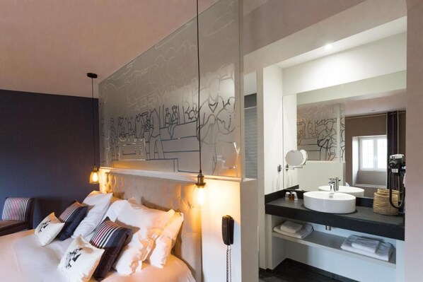 A modern hotel room with a large bed, a bedside telephone, a bathroom with a sink and mirror, and wall art. - Logis Hotel Du Fronton-agian (Itxassou)